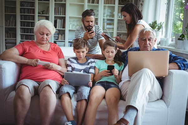 Multi-generation family sitting on sofa and using laptop, mobile phone and digital tablet