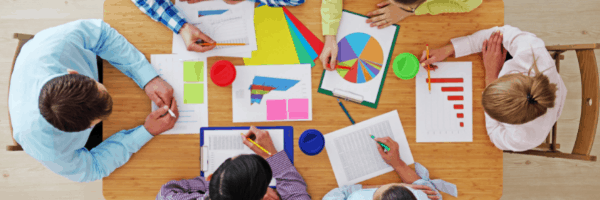 group of marketers sitting down at a round table looking at bar graphs and quarterly reports.