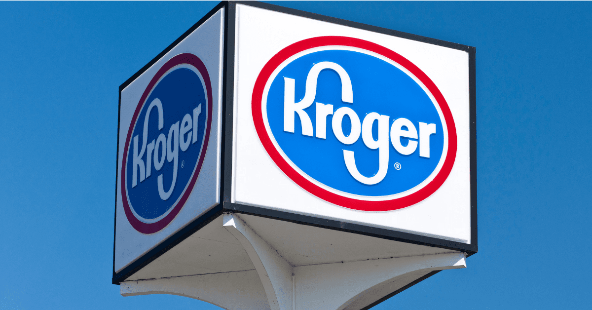Ein Kroger-Schild mit dem blau-roten Firmenlogo auf weißem Hintergrund, das an einem weißen Pfosten vor strahlend blauem Himmel angebracht ist, kennzeichnet den Standort dieses beliebten Kroger-Supermarkts.