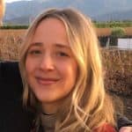 Eine junge Frau mit langen blonden Haaren lächelt im Freien, vor dem Hintergrund von Weinbergen und Bergen unter einem klaren Himmel – ein Moment, der so erfrischend und beeindruckend ist wie die Incrementalität von Retail Media.
