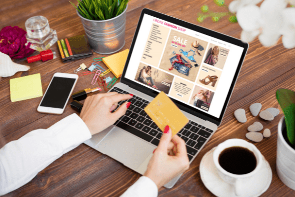 Woman sitting down at her desk browsing a retail fashion sale with her credit card in hand.