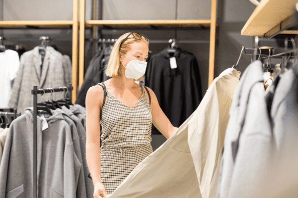 Older woman with a KN95 mask looking at a selection of clothes in a department store.