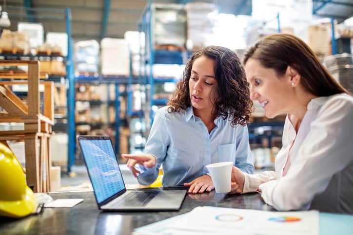 Two business women looking at a laptop and discussing their Walmart advertising strategy in their warehouse.