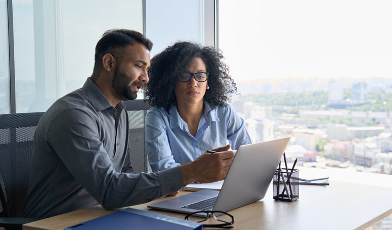 A businessman and a business woman looking at a laptop and discussing their Walmart advertising strategy.