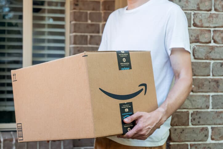 Une personne en tee-shirt tient une boîte de livraison Amazon.