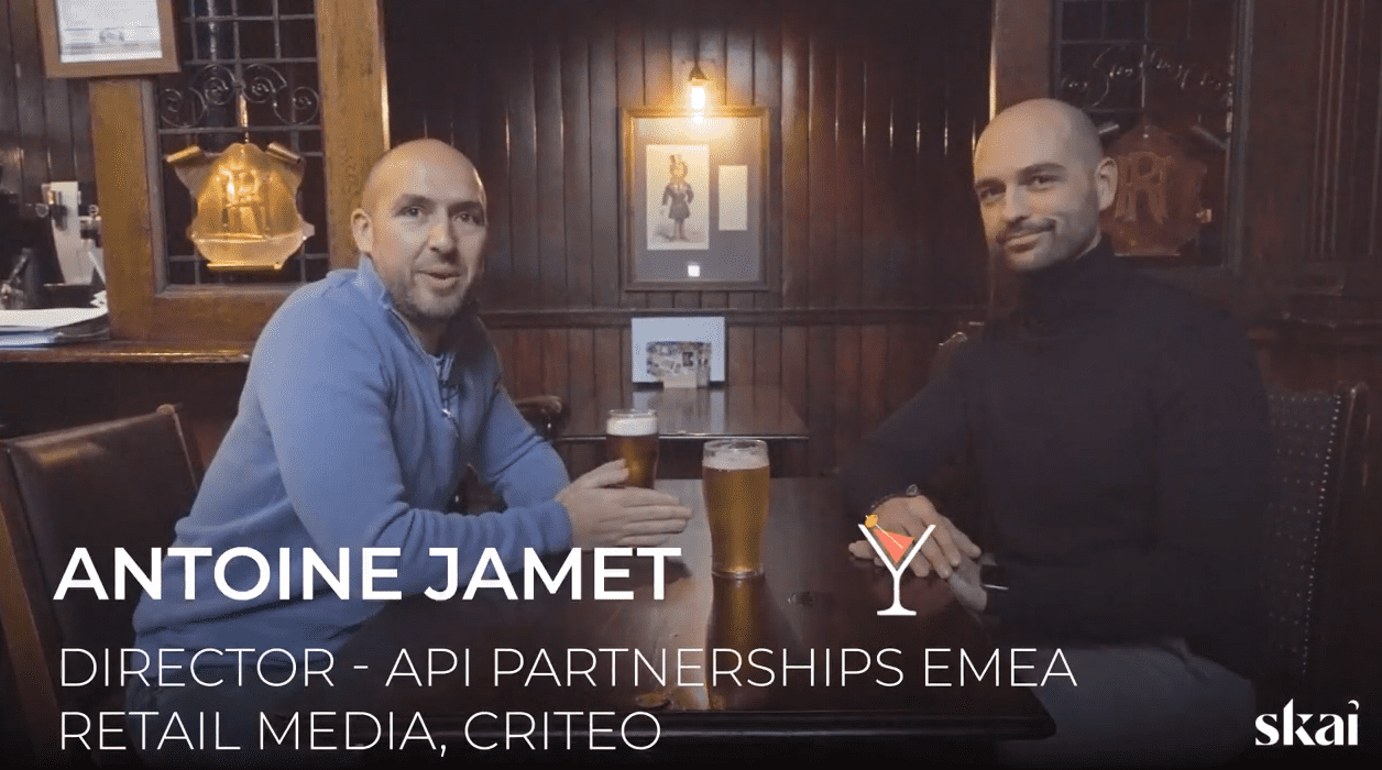 Deux hommes sont assis à une table en bois dans un pub, chacun avec une pinte de bière. Le texte sur l'image indique : Antoine Jamet, directeur des partenariats API EMEA, Retail Media, Criteo. Le Skai apparaît dans le coin inférieur droit, soulignant le rôle d'Antoine Jamet.