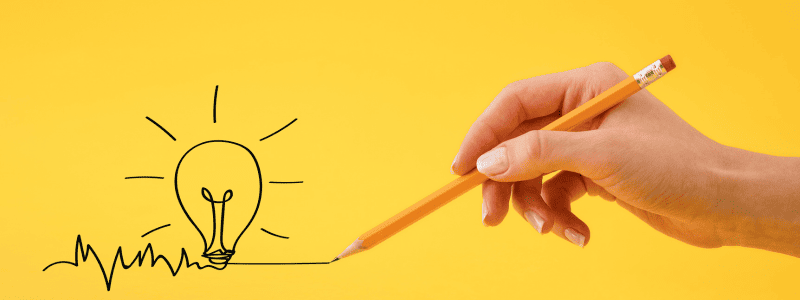 A hand holds a pencil, drawing a continuous line that forms a light bulb with rays, symbolizing a creative idea, against a bright yellow background.