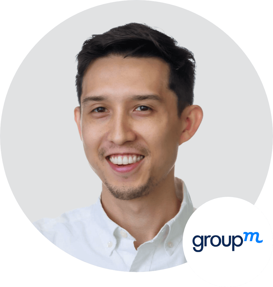 A smiling man with short dark hair and a trimmed beard wearing a white collared shirt, pictured in front of a light gray background. The GroupM logo is in the lower right corner.