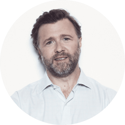 A man with brown hair and a beard, wearing a light-colored dress shirt, smiles slightly while looking at the camera against a plain white background—perfect for a retail media advertising case study.