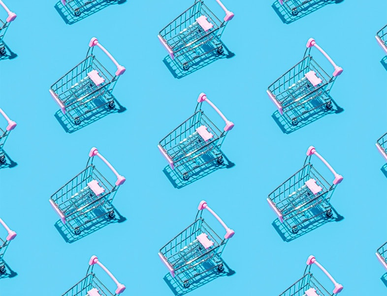 Mehrere kleine Einkaufswagen mit rosa Griffen sind diagonal auf einem leuchtend blauen Hintergrund angeordnet und werfen Schatten nach rechts – eine spielerische Anspielung auf Retail Media 2025 und die Zukunft des Einkaufserlebnisses.