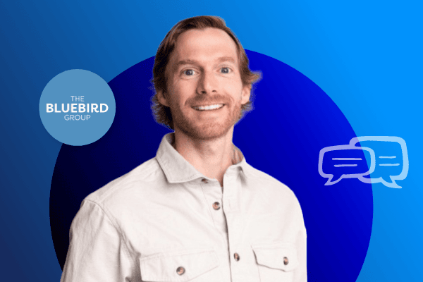 Ein lächelnder Mann mit hellbraunen Haaren und Bart trägt ein hellbeiges Hemd und steht vor einem blauen Hintergrund mit dem Logo von THE BLUEBIRD GROUP und zwei Sprechblasen-Symbolen – bereit, über die neuesten Tarife im Bereich Retail Media zu sprechen.