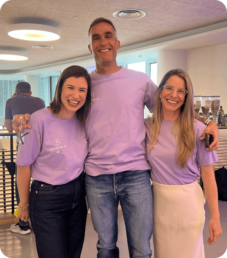 Trois personnes se tiennent côte à côte à l'intérieur et sourient à la caméra. Elles portent toutes des t-shirts lavande assortis et semblent heureuses. En arrière-plan, on aperçoit une pièce moderne et bien éclairée, avec des fenêtres et d'autres personnes en train de travailler.