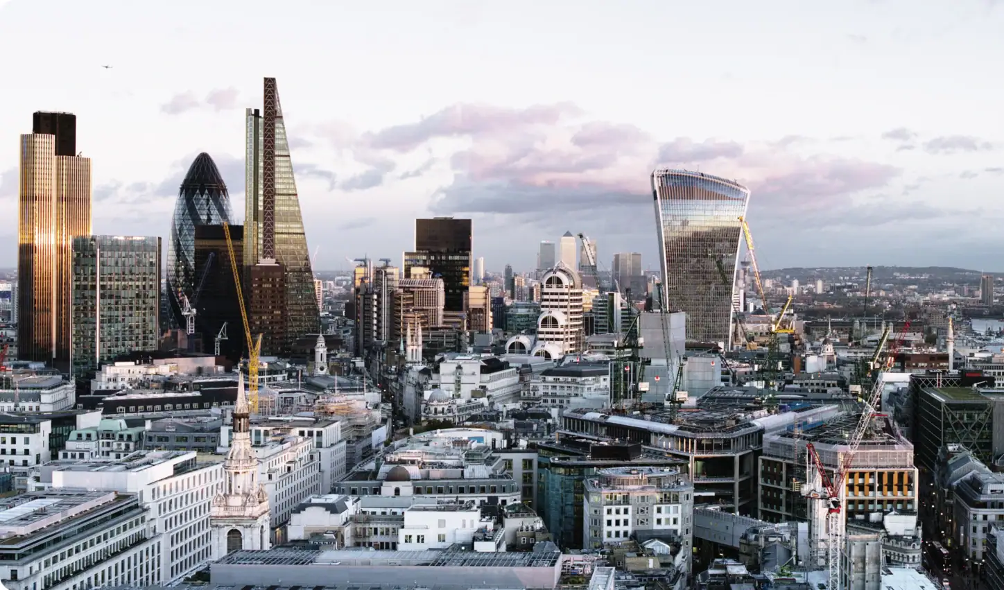 Une vue panoramique sur les toits de Londres, mettant en avant des gratte-ciel modernes tels que « The Gherkin », « The Shard » et « The Walkie Talkie », avec des bâtiments historiques au premier plan sous un ciel nuageux.
