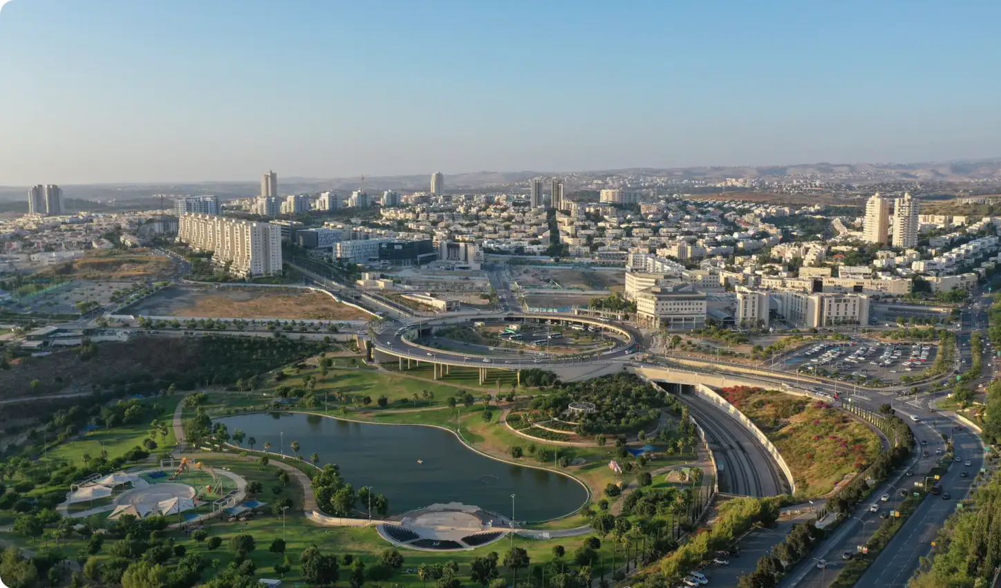 Vue aérienne d'une ville moderne avec de grands immeubles, de vastes quartiers résidentiels, des parcs verdoyants agrémentés d'étangs et un grand échangeur autoroutier, le tout sous un ciel bleu limpide.