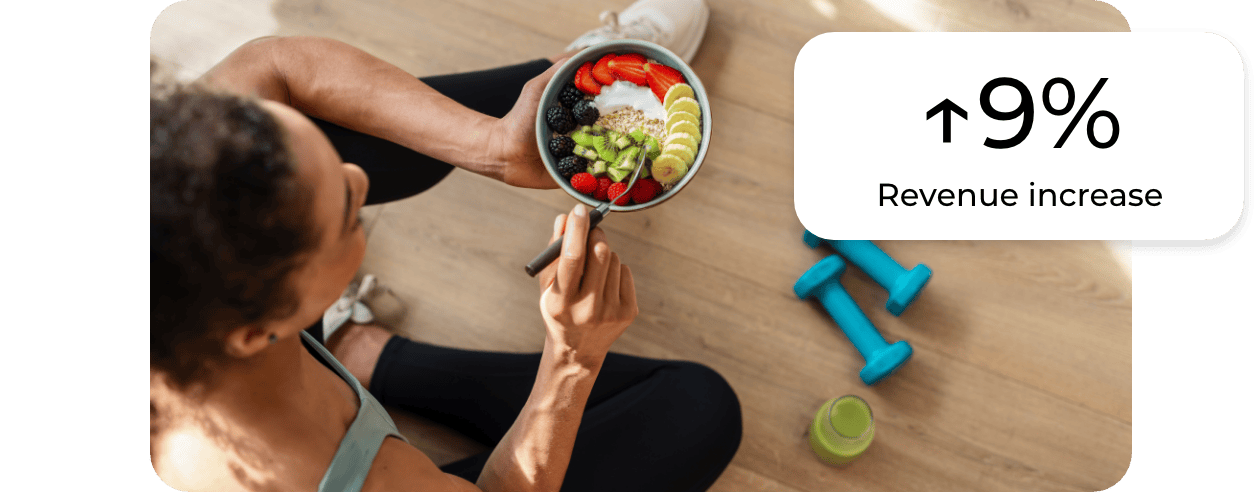 A person sits on the floor holding a bowl of assorted fruit. Two blue dumbbells and a green water bottle are nearby, emphasizing wellness powered by data centralization. A graphic overlay reads ↑9% Revenue increase.