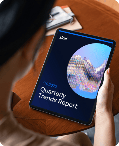 Eine Person hält ein Tablet in der Hand, auf dem ein Bericht mit dem Titel „Q4 2025 Quarterly Trends Report by Skai zu sehen ist, der eine farbenfrohe abstrakte Grafik und Einblicke in den Bereich Retail Media 2026 enthält. Die Person sitzt an einem Holztisch, im Hintergrund sind Papiere zu sehen.