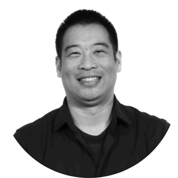 A man with short black hair is smiling, dressed in a dark collared shirt. Photographed against a plain white background, this black and white image reflects the clarity and focus that Data Centralization can bring to your organization.