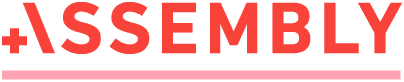 Auf dem Bild ist das Wort „ASSEMBLY“ in fetten, roten Großbuchstaben zu sehen, wobei vor dem Buchstaben A ein rotes Pluszeichen steht. Unter dem Text verläuft eine rote horizontale Linie. Der Hintergrund ist hellgrau.