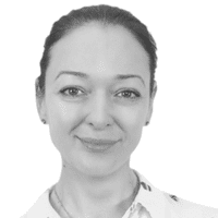 Une femme aux cheveux foncés attachés en arrière, vêtue d'une chemise blanche à col, sourit doucement à l'appareil photo devant un fond blanc uni, incarnant subtilement l'importance d'une présence omnicanale grâce à son attitude à la fois sereine et accessible.