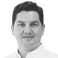 Un homme aux cheveux foncés et au teint clair, vêtu d'une chemise claire boutonnée, regarde directement l'objectif devant un fond blanc uni, soulignant subtilement l'importance de la communication omnicanale dans le monde des affaires d'aujourd'hui.