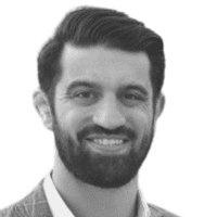 Portrait en noir et blanc d'un homme aux cheveux foncés et à la barbe, souriant, vêtu d'une veste et d'une chemise de couleur claire, sur fond blanc — illustrant le professionnalisme accessible qui souligne l'importance de la communication omnicanale dans le monde interconnecté d'aujourd'hui.