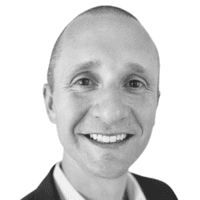 Une personne souriante, au crâne rasé, vêtue d'une veste de costume et d'une chemise à col, photographiée en noir et blanc sur fond blanc, incarnant l'importance du professionnalisme omnicanal dans le monde des affaires d'aujourd'hui.