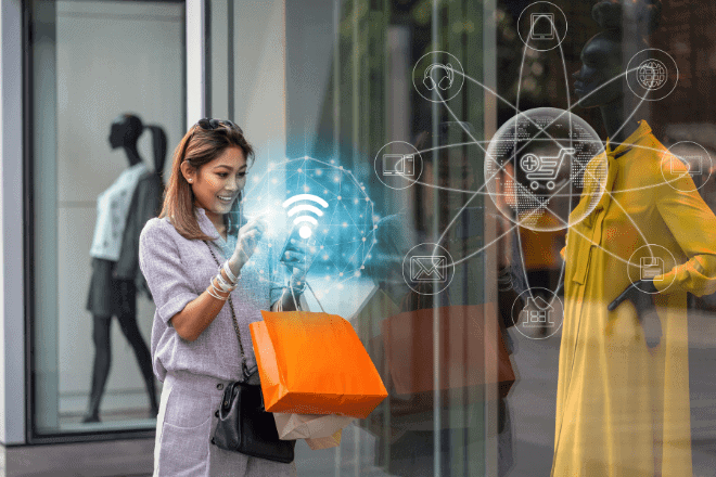 Une femme tenant des sacs de courses utilise son smartphone devant un magasin. Des icônes représentant le commerce en ligne et Internet apparaissent en superposition, symbolisant les achats en ligne ou les technologies de vente au détail connectées, et soulignant l'importance des expériences omnicanales dans le commerce de détail moderne. On aperçoit des mannequins dans la vitrine.