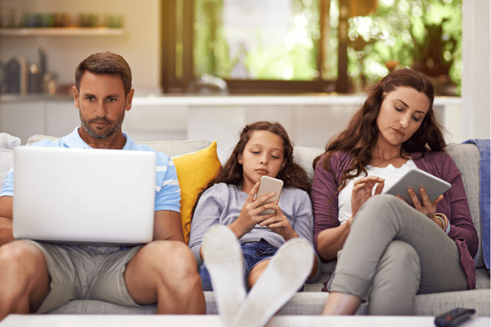 Un homme, une jeune fille et une femme sont assis sur un canapé, chacun utilisant un appareil : un ordinateur portable, un smartphone et une tablette. Ils semblent concentrés sur leurs écrans et n'interagissent pas entre eux, illustrant ainsi l'expérience client omnicanale moderne, dans laquelle les individus interagissent de manière fluide sur plusieurs plateformes numériques.