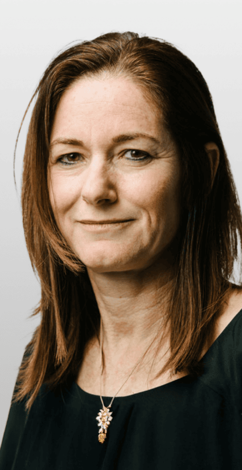 Porträtfoto einer Frau mittleren Alters mit schulterlangem braunem Haar, die ein dunkles Shirt und eine Halskette mit Anhänger trägt.